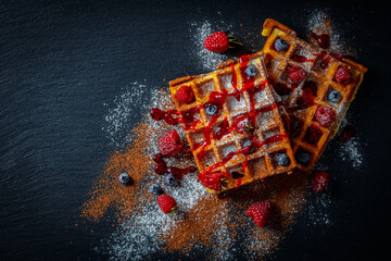 Fresh baked berry Belgian waffle with raspberries and blueberries on black a plate for breakfast, closeup, top view. Culinary, cooking, bakery concept. Food recipe background. Sweet waffles