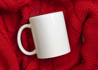 White blank coffee mug on red knitted sweater top view, Christmas winter Holiday mockup