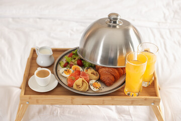 Tray with delicious breakfast on bed in hotel room, closeup