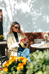 Woman using her phone while sitting outdoors at a cafe on a sunny day