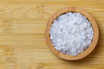Natural sea salt, scattered in a wooden bowl, on a wooden background.
