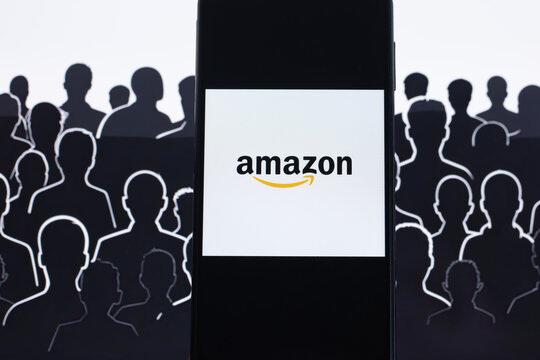 Amazon logo is displayed on a smartphone with the silhouette of workers in the background.