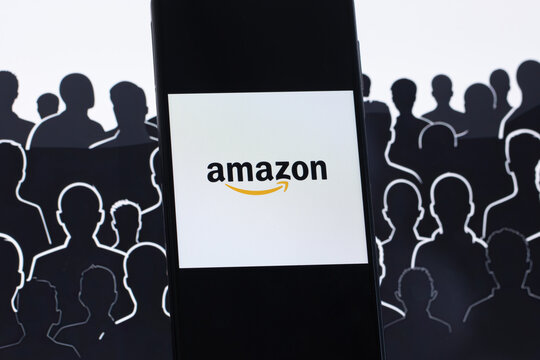 Amazon logo is displayed on a smartphone with the silhouette of workers in the background.