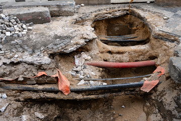 Deep Trench Revealing Underground Utility Pipes in City.
