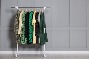 Different clothes hanging on rack near grey wall indoors. Space for text