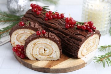 Delicious Yule log (traditional Christmas cake) with redcurrant and fir tree branches on white table, closeup