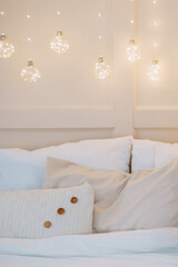 Cozy bedroom adorned with Christmas fairy lights glowing above a bed with white and beige pillows. Holiday interior decor concept.