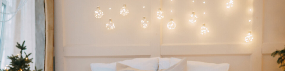 Christmas tree decorated with festive lights and ornaments beside a wall adorned with string...