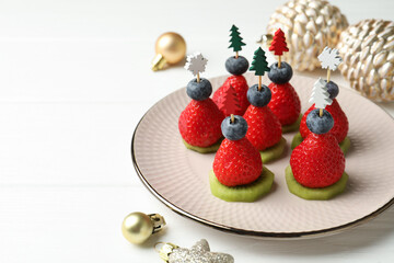 Christmas food. Tasty canapes with strawberries, kiwi, blueberries and decor on white wooden table,...