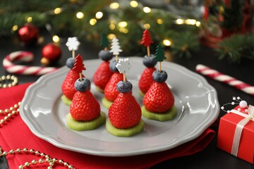 Christmas food. Tasty canapes with strawberries, kiwi, blueberries and decor on black table,...