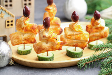 Tasty snacks with puff pastry, olives, cucumber and Christmas decor on grey textured table, closeup
