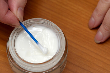 Applying cream with a cotton swab on a wooden surface