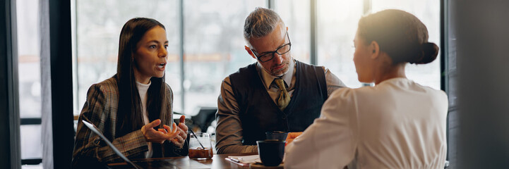 Three dedicated professionals are engaged in a serious discussion while enjoying coffee at a chic, trendy cafe