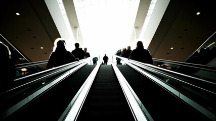 Silhouetted figures descend an escalator, creating a dramatic contrast against bright light. This image captures the essence of movement and urban life in public spaces.