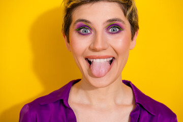 Playful young woman sticks out tongue and smiles brightly against a bold yellow background wearing...