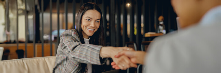 A professional woman in a stylish blazer confidently shaking hands within a contemporary corporate...
