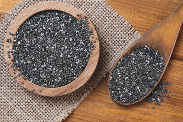 Chia seeds in a wooden spoon, a bowl full with a mound of chia seeds. 