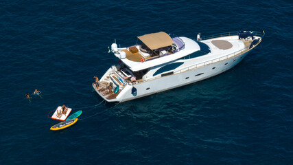Aerial closeup of a yacht with people on vacation. There are two stand-up paddleboards and a...