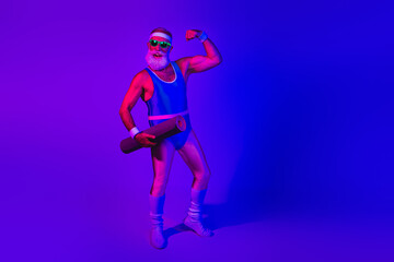 Retro fitness model with blue jumpsuit under neon purple lighting flexing arm and holding a mat in a studio portrait