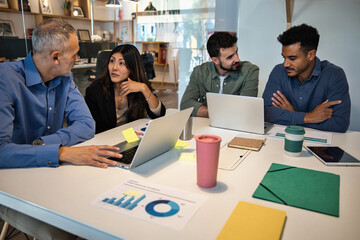 Diverse business team collaborating at a meeting table with laptops and charts. Professionals working together on company strategy. Business concept.