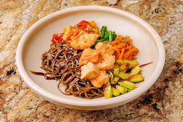 Delicious soba noodles with salmon and vegetables served on a ceramic plate. Asian cuisine, healthy food with teriyaki sauce and sesame seeds.