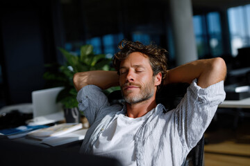 Fototapeta premium A relaxed man leans back in an office chair with eyes closed, embodying a sense of serenity and contentment in a well-lit indoor workspace filled with greenery.