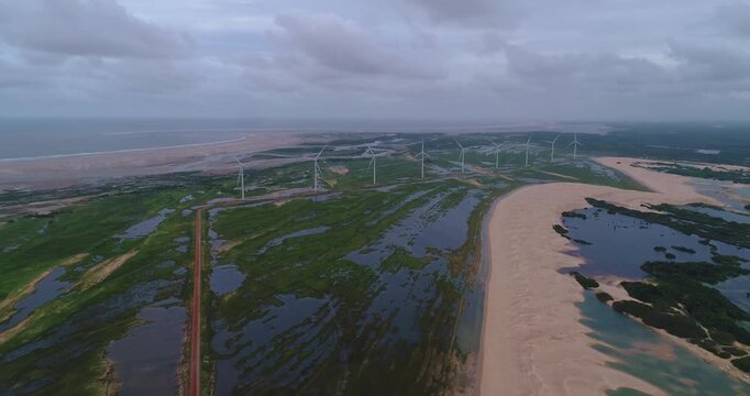 Dunas e lagoas dos Pequenos Len&ccedil;&oacute;is Maranhenses com turbinas e&oacute;licas girando ao fundo, capturadas por drone em Paulino Neves, Maranh&atilde;o, mar praia