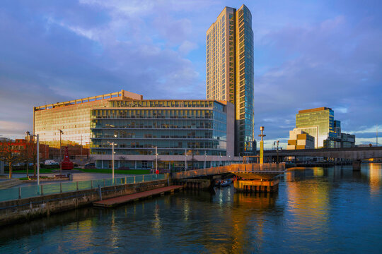 Belfast evening skyline with tall buildings and a dramatic sky over the River Lagan, viewed from the historic Lagan Weir Bridge in Northern Ireland.