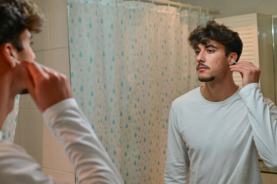 man cleaning ear with cotton swab at bathroom