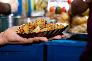 Bengali woman holding plate of alu kabli street food at roadside snacks stall in Kolkata
