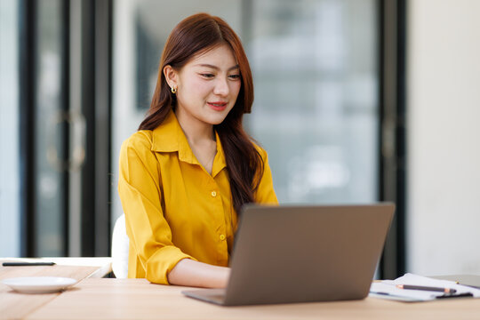 Smiling woman analyzing financial data graphs, charts on laptop display at a modern workspace. Financial analysis or business evaluation concept
