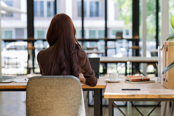 Back side view of Asian freelance woman typing on keyboard and working on laptop woman working for...