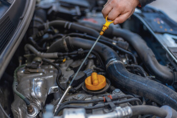 Fototapeta premium A close-up of a person's hand removing the oil dipstick from the engine. Routine maintenance, self-diagnosis, car care. The hand and the yellow dipstick are the main focus. Checking the oil level.