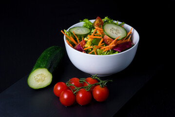 Ensalada vegana con tomate lechuga zanahoria pepino en un bol con fondo oscuro