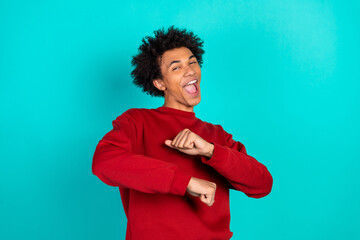 Energetic young man in red sweater dancing with joy against teal blue background for lifestyle fashion advertising and stock photo