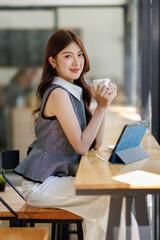 attractive young asian woman drink coffee and holding digital tablet screen in cafe business concept.
