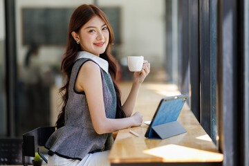 attractive young asian woman drink coffee and holding digital tablet screen in cafe business concept.

