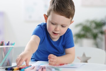 Cute little boy with felt pen drawing at white table indoors