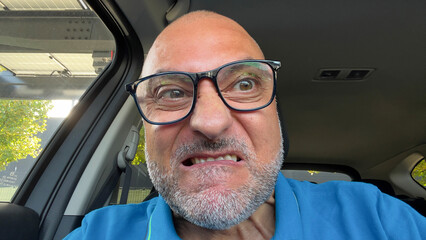 A middle aged man shows strong anger while driving his car expressing frustration during a stressful moment on the road.