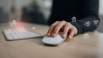 Close-up of a person's hand using a computer mouse and keyboard with glowing digital icons floating in the air representing technology and connectivity