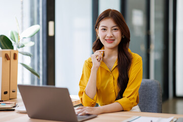 Smiling asian woman looking at camera in front of computer Office casual image Cute woman in pink...
