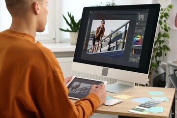 Professional retoucher editing photo on computer and tablet at table in office, back view