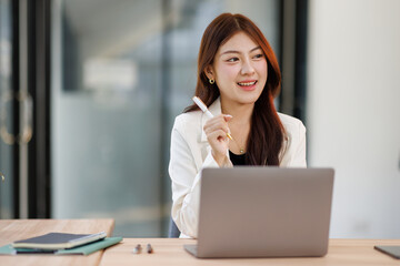 Smiley young business asian woman holding business plan note and sitting at desk in modern coworking office.
