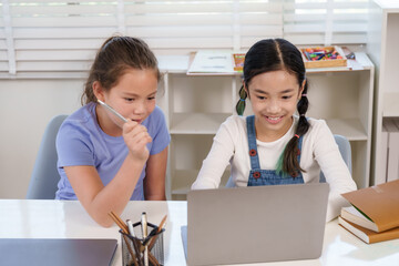 Caucasian schoolgirl preteen holding pencil thinking beside asian classmate laptop classroom teamwork project study homework education learning cooperation childhood