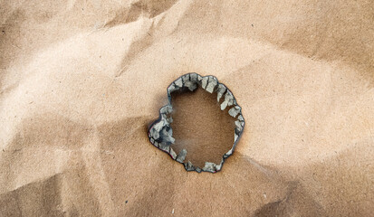 Burned Hole on Brown Cardboard background. This dark, charred hole texture is ideal for grunge, damage, and abstract design overlays