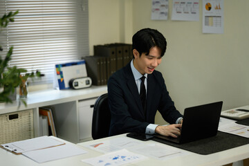 A Young Asian Businessman Working on Laptop at Office Desk