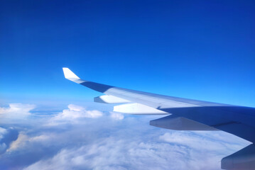View of airplane wing above clouds on a clear sunny day with blue sky