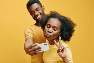 Young African couple taking a selfie together against a bright yellow background, showcasing playful emotions and vibrant fashion, ideal for social media content
