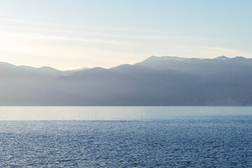 Calm blue ocean with hazy mountains under clear sky at sunrise