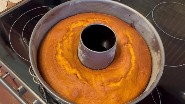 Freshly baked orange cake rises in a round pan, showcasing its golden crust and smooth texture, as the camera performs a slow zoom in to capture the details